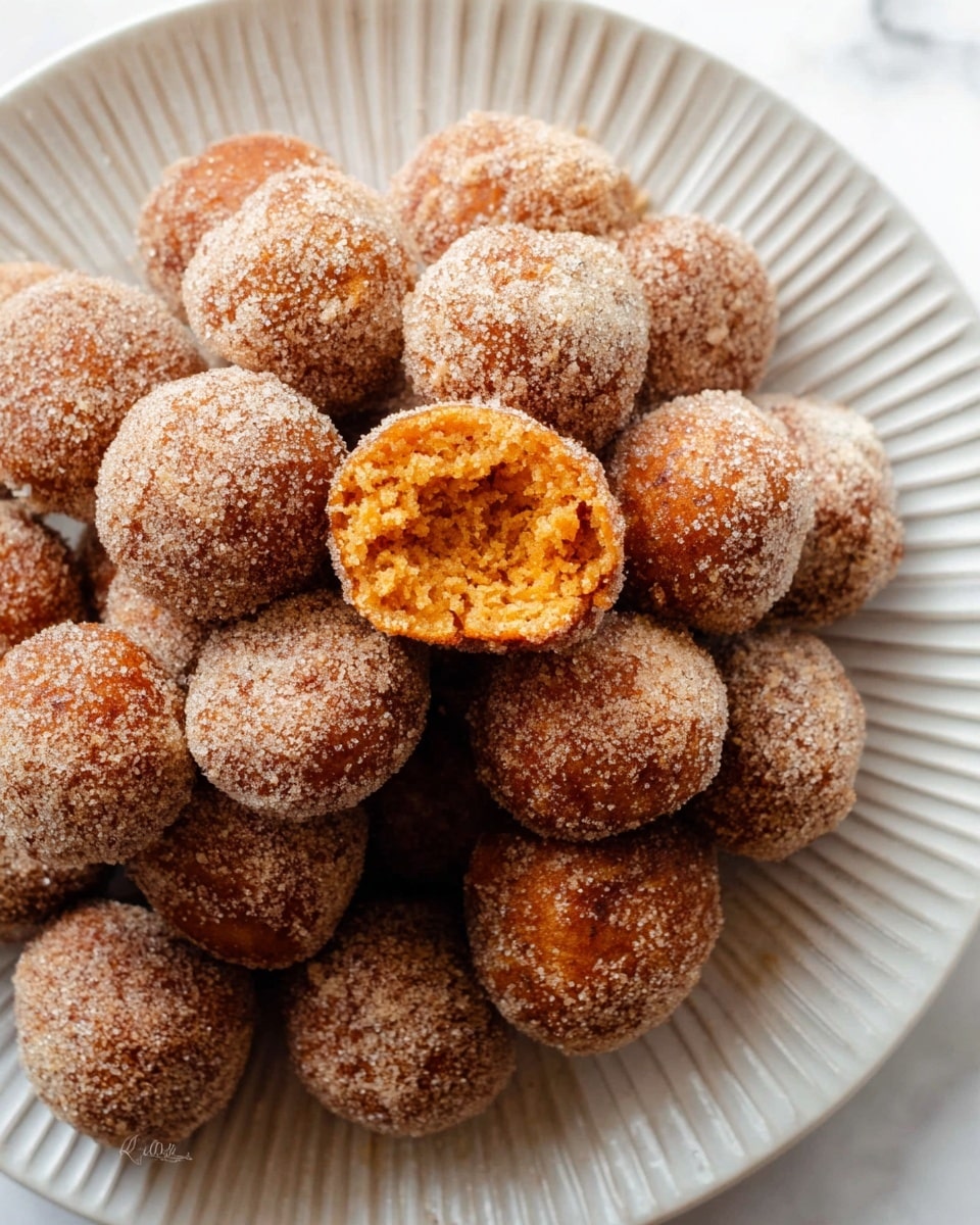 A white plate with ridged edges is filled with many round, small doughnut balls covered in a brown sugary coating. One doughnut ball is split open at the front, showing a fluffy, orange interior with a soft texture. The doughnut balls are piled up closely on the plate, which sits on a white marbled surface. photo taken with an iphone --ar 4:5 --v 7