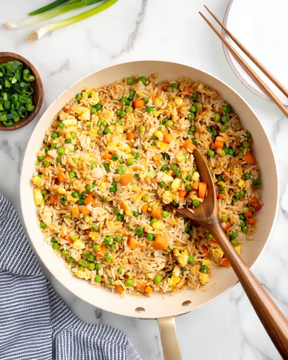 A white pan filled with three layers of fried rice, mixed evenly with small bright green peas, orange carrot cubes, and bits of scrambled yellow egg. A wooden spoon is scooping some rice from the middle, showing the mix of ingredients clearly. To the left, there is a small wooden bowl with chopped green onions, and to the right, a white plate with brown chopsticks resting on its edge, all placed on a white marbled surface with a striped cloth near the bottom left. Photo taken with an iphone --ar 4:5 --v 7