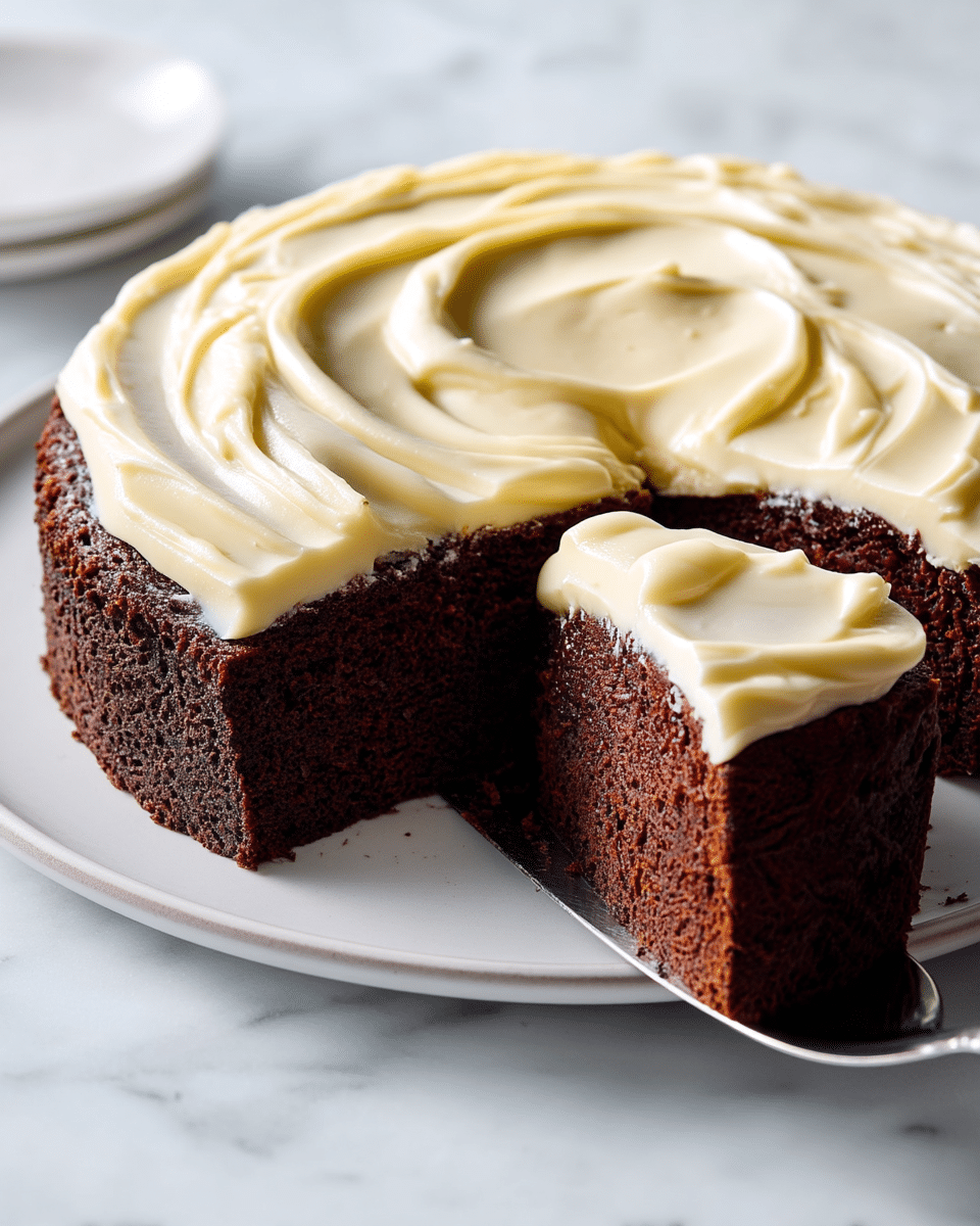 A single-layer round chocolate cake sits on a white plate, topped thickly with creamy pale yellow frosting that has smooth swirls and a soft texture. A slice has been cut out and is being lifted by a silver cake server, showing the moist, dark brown crumb inside. The white marbled background adds a clean and simple look to the scene. Photo taken with an iphone --ar 4:5 --v 7