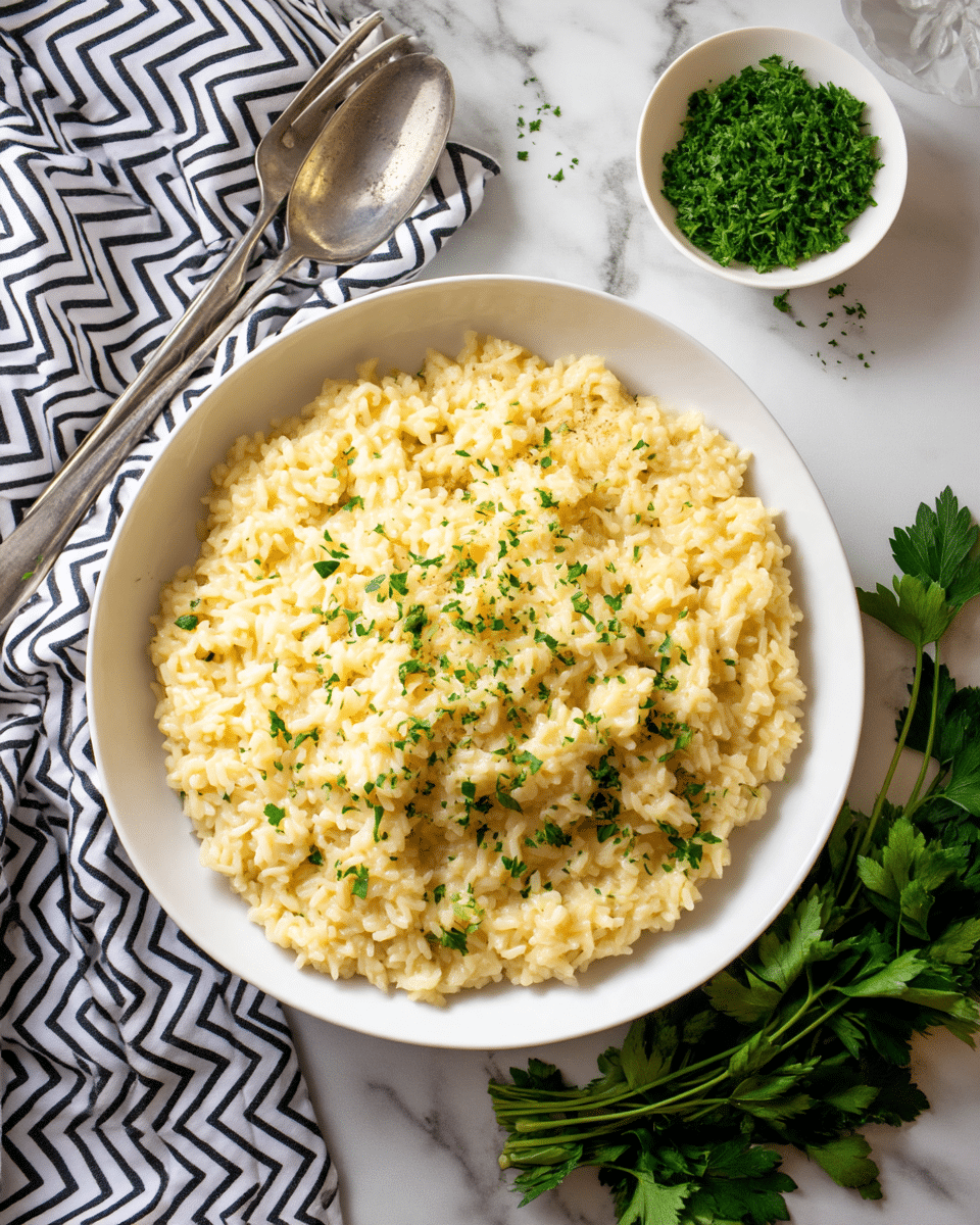 A large white bowl filled with one layer of creamy, light yellow risotto, topped with small sprinkles of chopped green herbs. The risotto has a soft, slightly wet texture with visible grains of rice. Around the bowl, on a white marbled surface, there is a whole bunch of flat green parsley leaves in the bottom right corner and a small white bowl with finely chopped green herbs in the upper left corner. To the left of the bowl, a black and white chevron patterned cloth lies partially under it, with a worn metallic serving spoon resting on top. In the background, two stacked white bowls with silver forks inside are slightly out of focus, with the whole scene softly lit. photo taken with an iphone --ar 4:5 --v 7