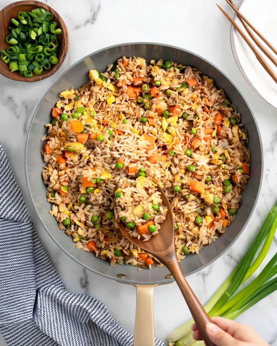 A large gray pan filled with fried rice that has three visible layers: a base layer of light brown cooked rice mixed with small pieces of bright orange carrot, green peas, and scrambled yellow egg bits, all evenly spread. A wooden spoon is scooping a portion of the rice, showing the mixed colors and soft textures. Surrounding the pan on a white marbled surface are a small wooden bowl filled with chopped green onions to the left, a white plate with wooden chopsticks to the right, and a bunch of long green onions at the bottom right. A white and black striped cloth is partly visible under the pan's handle. Photo taken with an iphone --ar 4:5 --v 7