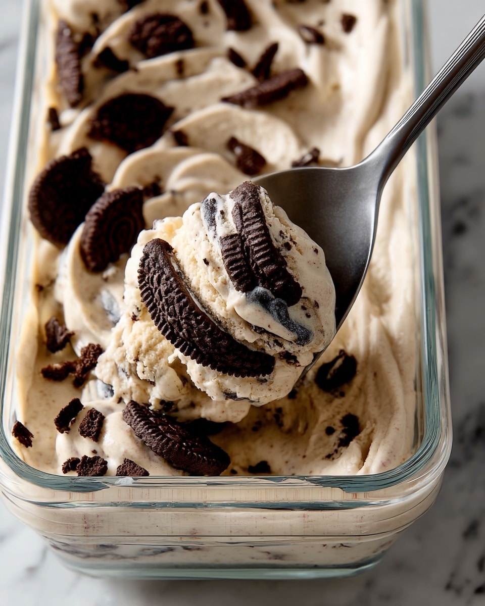 A close-up view of creamy, light beige ice cream mixed with many large and small dark chocolate cookie chunks, swirling thickly in a clear glass container. The ice cream has a smooth, soft texture with bits of cookie embedded throughout. A dark metal spoon lifts a generous scoop of the ice cream, showing dense cookie pieces in every bite. The scene is set on a white marbled surface, highlighting the contrast between the creamy ice cream and dark cookies. photo taken with an iphone --ar 4:5 --v 7