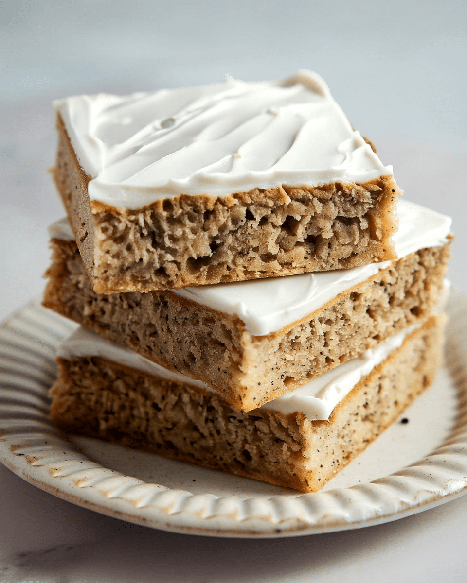 A stack of three square pieces of a light brown cake with a moist and slightly crumbly texture, each piece topped with a smooth, thick layer of white frosting that has subtle spread marks. The bottom cake layer shows small dark specks, suggesting nuts or spices inside. The slices are arranged slightly tilted on a white plate with a ridged edge, set on a white marbled surface that adds a clean and bright background to the image. Photo taken with an iphone --ar 4:5 --v 7