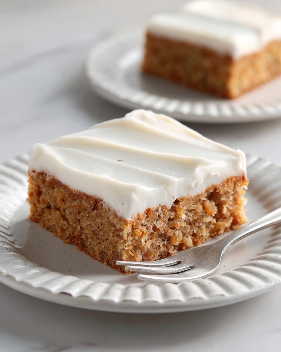 A square piece of cake with two layers is on a white plate with ridged edges. The bottom layer is light brown with a slightly rough and crumbly texture, showing small bits inside the cake. The top layer is smooth white frosting spread evenly with gentle waves. A silver fork is placed under the cake on the plate. The background is a white marbled surface, and another piece of the cake is visible blurred in the background. photo taken with an iphone --ar 4:5 --v 7
