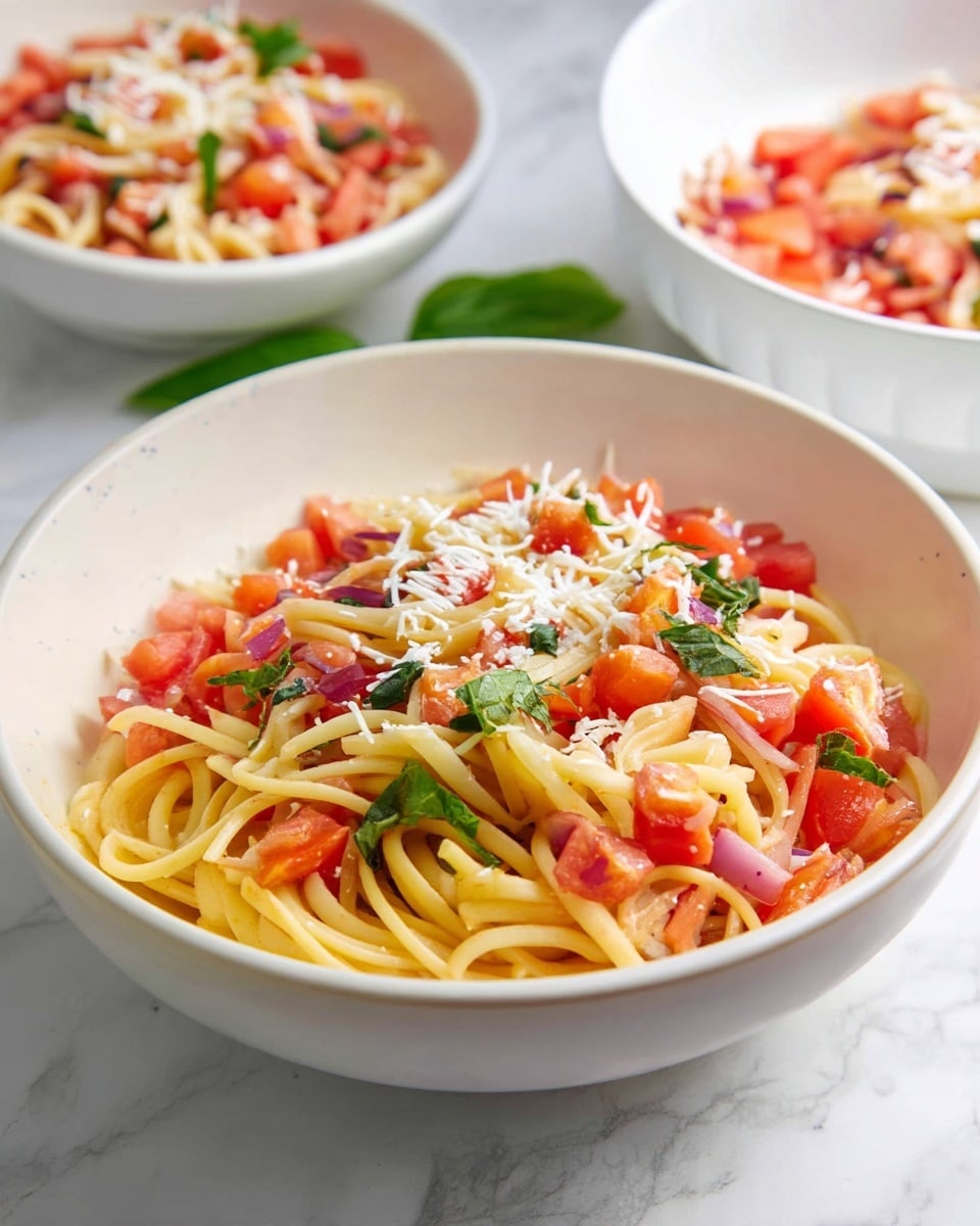 A white bowl filled with three layers: the bottom layer is light yellow cooked spaghetti noodles, the middle layer has bright red diced tomatoes with small purple onion pieces and green basil leaves mixed throughout, and the top layer is sprinkled with shredded white cheese giving a fine texture across the dish. The bowl is placed on a white marbled surface with two other similar bowls slightly blurred in the background. Photo taken with an iphone --ar 4:5 --v 7