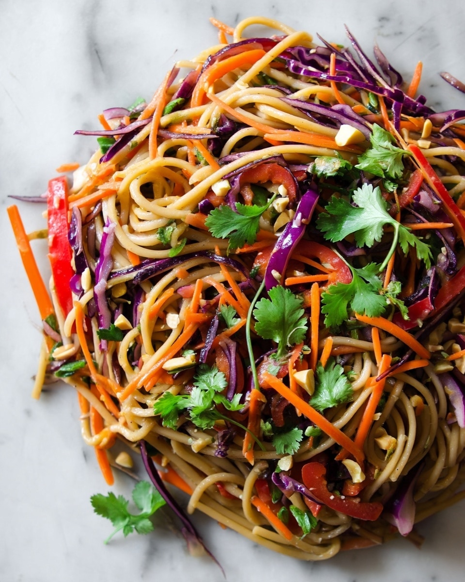 This dish shows a colorful mixture of thick beige noodles as the base layer, with thin strips of bright orange carrots and deep purple cabbage scattered throughout. There are also slices of vibrant red bell peppers mixed in. Fresh green cilantro leaves sit on top in small bunches, and small pieces of chopped nuts add texture all over. The dish is presented on a white marbled surface. photo taken with an iphone --ar 4:5 --v 7